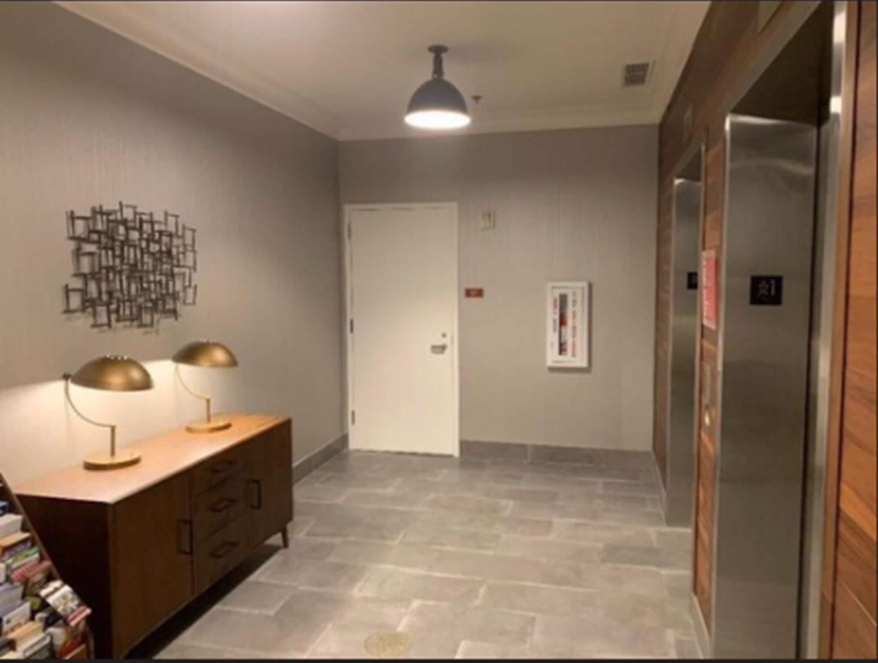 A hallway with a wooden cabinet, two floor lamps, a wall art piece, and a door.