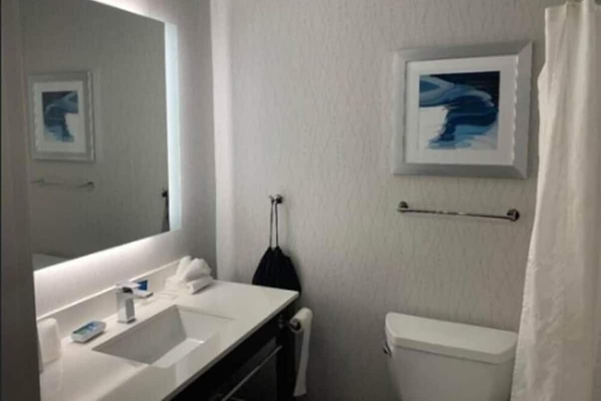 A bathroom with a white sink, mirror, and toilet. There is a towel rack with a towel hanging on it.
