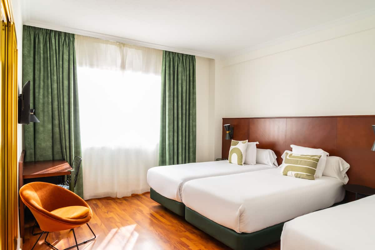 A hotel room with two beds, a desk, a chair, and a television.