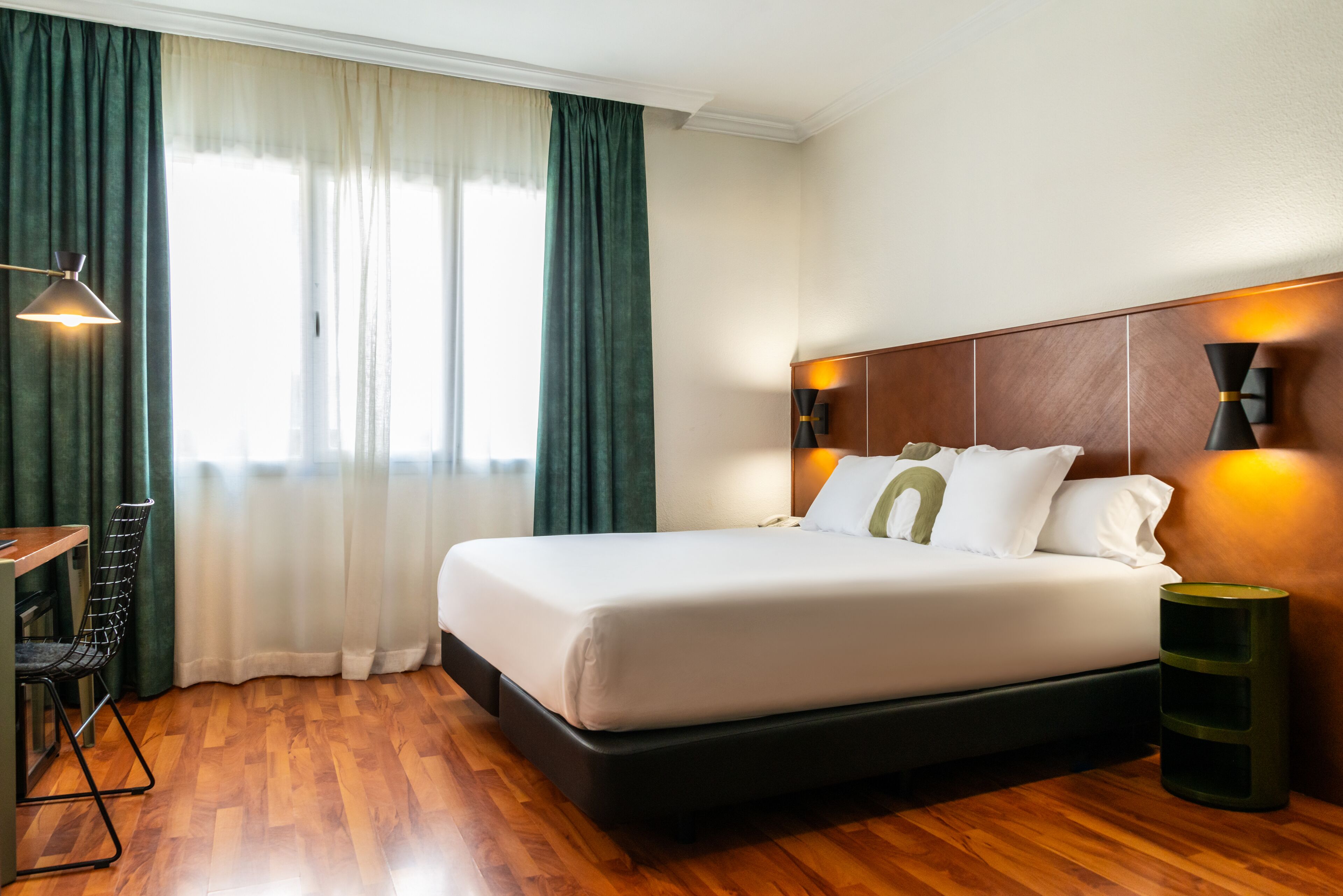 Una habitación de hotel con una cama grande, un escritorio con una silla, una lámpara y una mesita de noche.