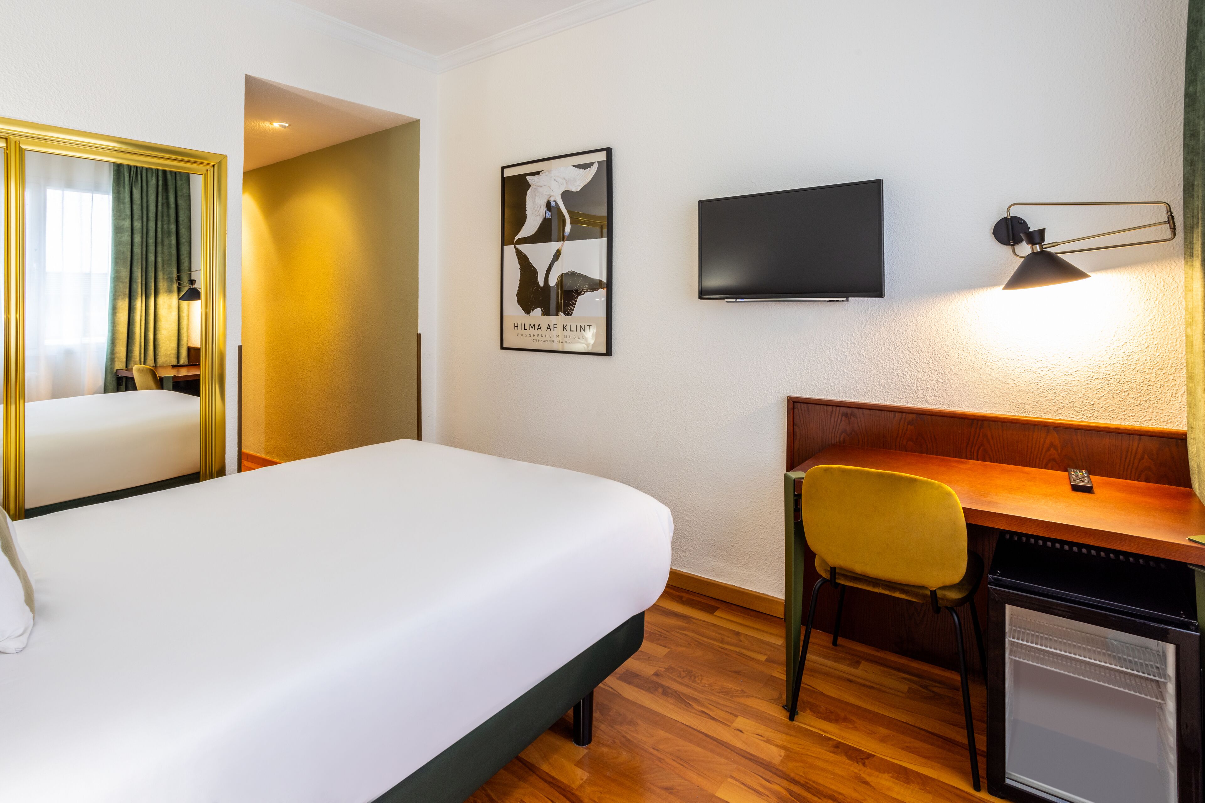 Una habitación de hotel con cama, escritorio, silla, televisor y refrigerador pequeño.