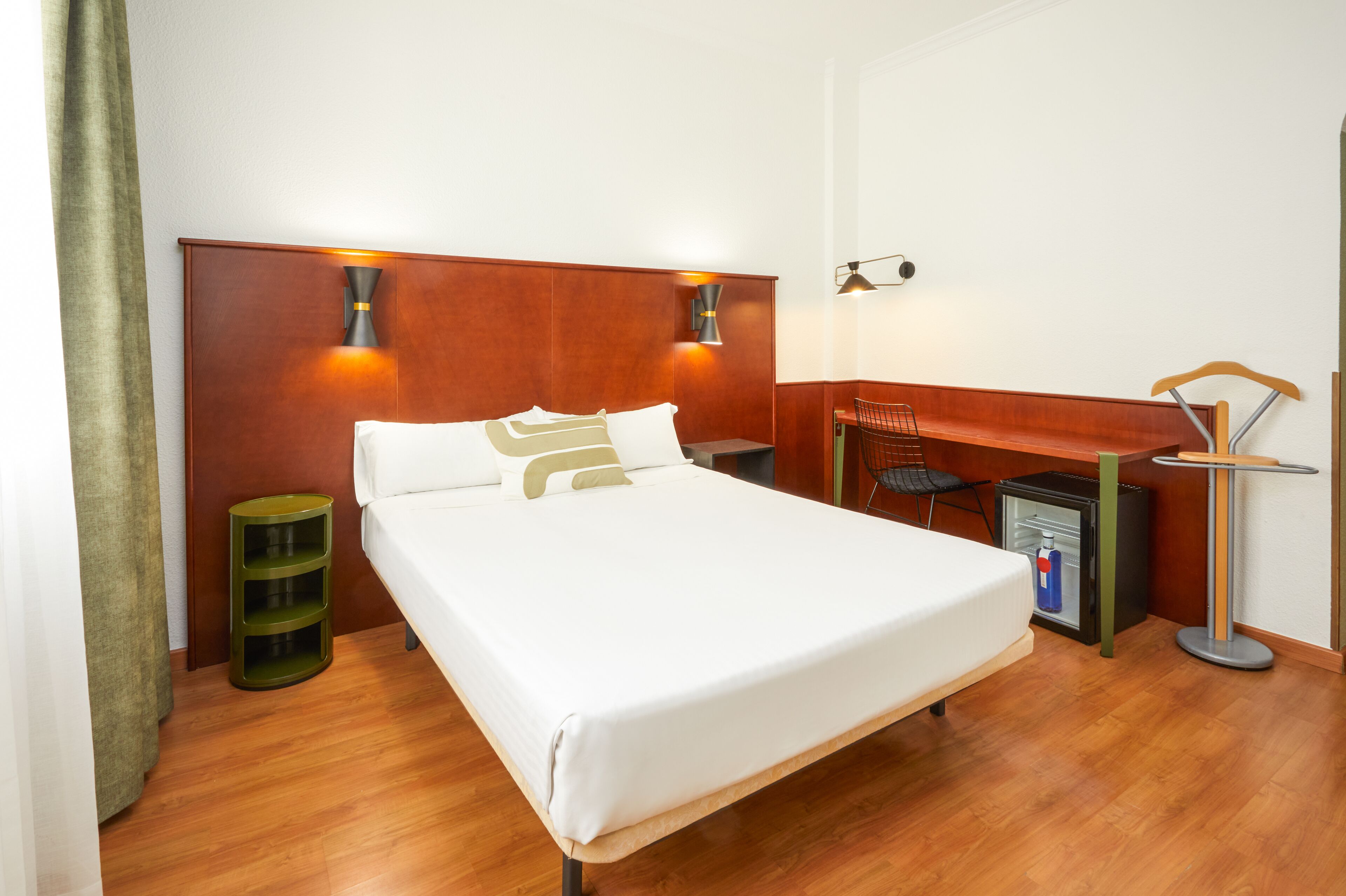Une chambre d’hôtel comprenant un lit, des tables de chevet, un bureau, une chaise et un petit réfrigérateur.