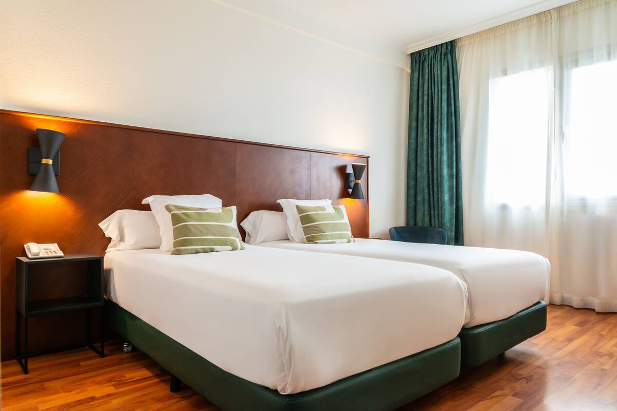 A double bed with white linens and green striped pillows, a wooden headboard, bedside lamps, and a telephone on a nightstand.