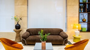 A modern living room with a brown sofa, two orange chairs, a glass coffee table, and a hanging light fixture. - Hôtel Casón del Tormes by HappyCulture (Madrid)