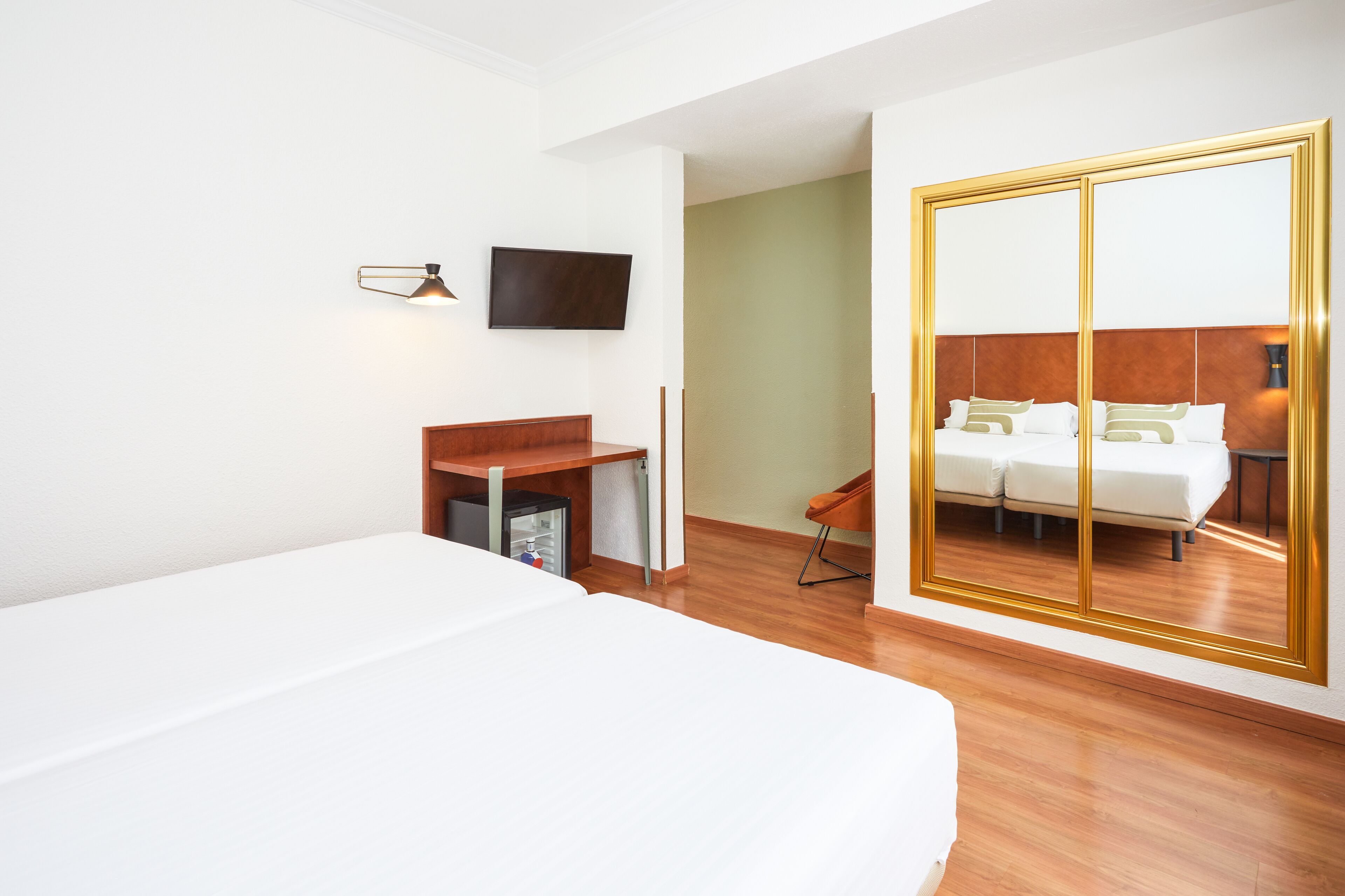 Habitación de hotel con una cama grande, un escritorio, una silla, un televisor y un armario con espejo.