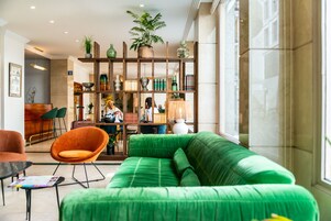 Um interior moderno com um sofá verde, uma poltrona laranja e uma estante de madeira com diversos objetos.