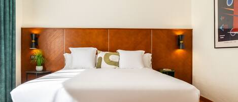 A neatly made bed with white linens and a green upholstered headboard. There are two wall-mounted lamps on either side of the bed.