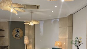 A modern hotel lobby with a seating area featuring a sofa, armchairs, and a coffee table. There are wicker ceiling fans and a large mirror on the wall. - Hôtel Casón del Tormes by HappyCulture (Madrid)