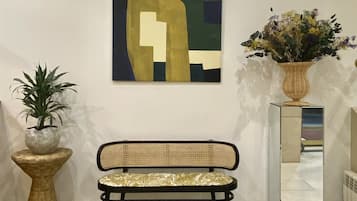 Un banco con respaldo tejido y asiento acolchado, una planta en maceta y un cuadro abstracto colgado en la pared.