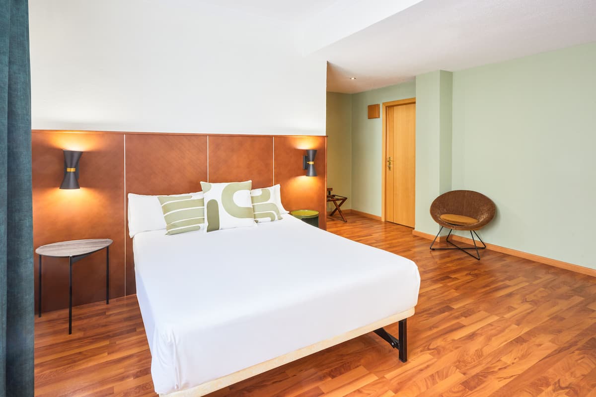 A neatly arranged bedroom with a large bed, two bedside lamps, a small round table, and a chair.