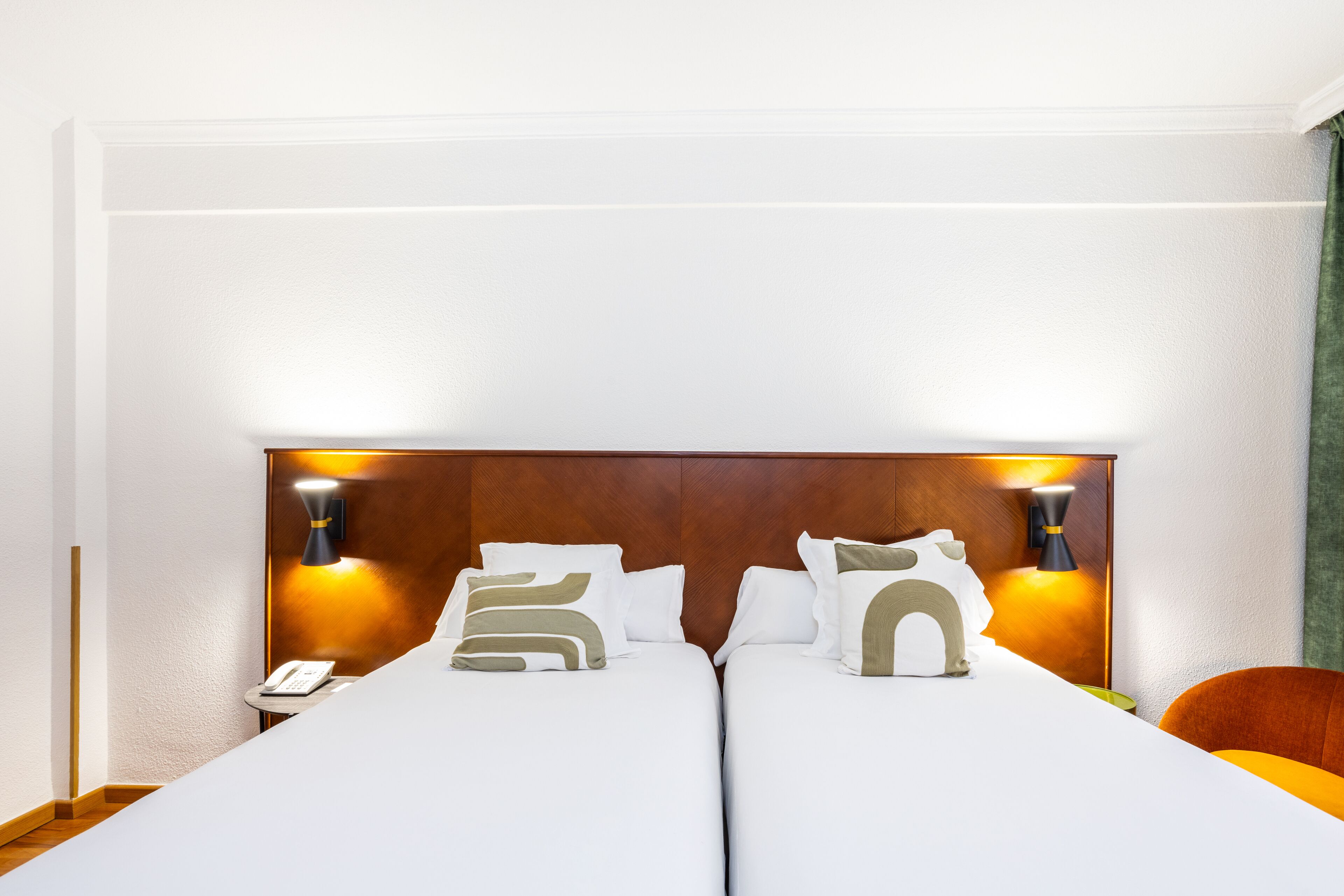 A double bed with white bedding and decorative pillows, two bedside lamps, and a wooden headboard.