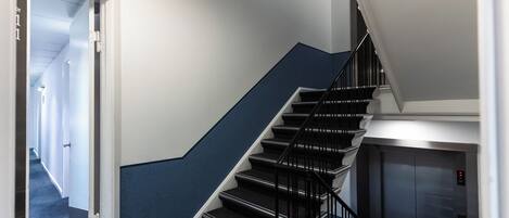 A staircase with a blue accent wall, a black railing, and an elevator to the right.