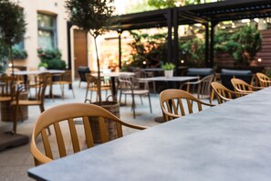An outdoor seating area with wooden chairs and tables, surrounded by greenery and a brick wall. - Go Hotel Ansgar (Copenhagen)