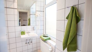 A modern bathroom with white tiled walls, a white sink, and a green towel hanging on the wall.