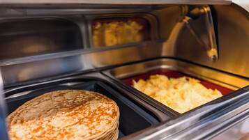 A buffet with a stack of pancakes and a container of scrambled eggs.