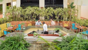Un vaste espace extérieur aménagé avec de nombreuses tables et chaises, entouré d’une végétation luxuriante et agrémenté d’une petite cascade.