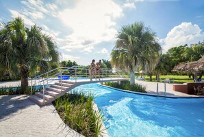 Una piscina con un puente, palmeras y sillas de descanso.