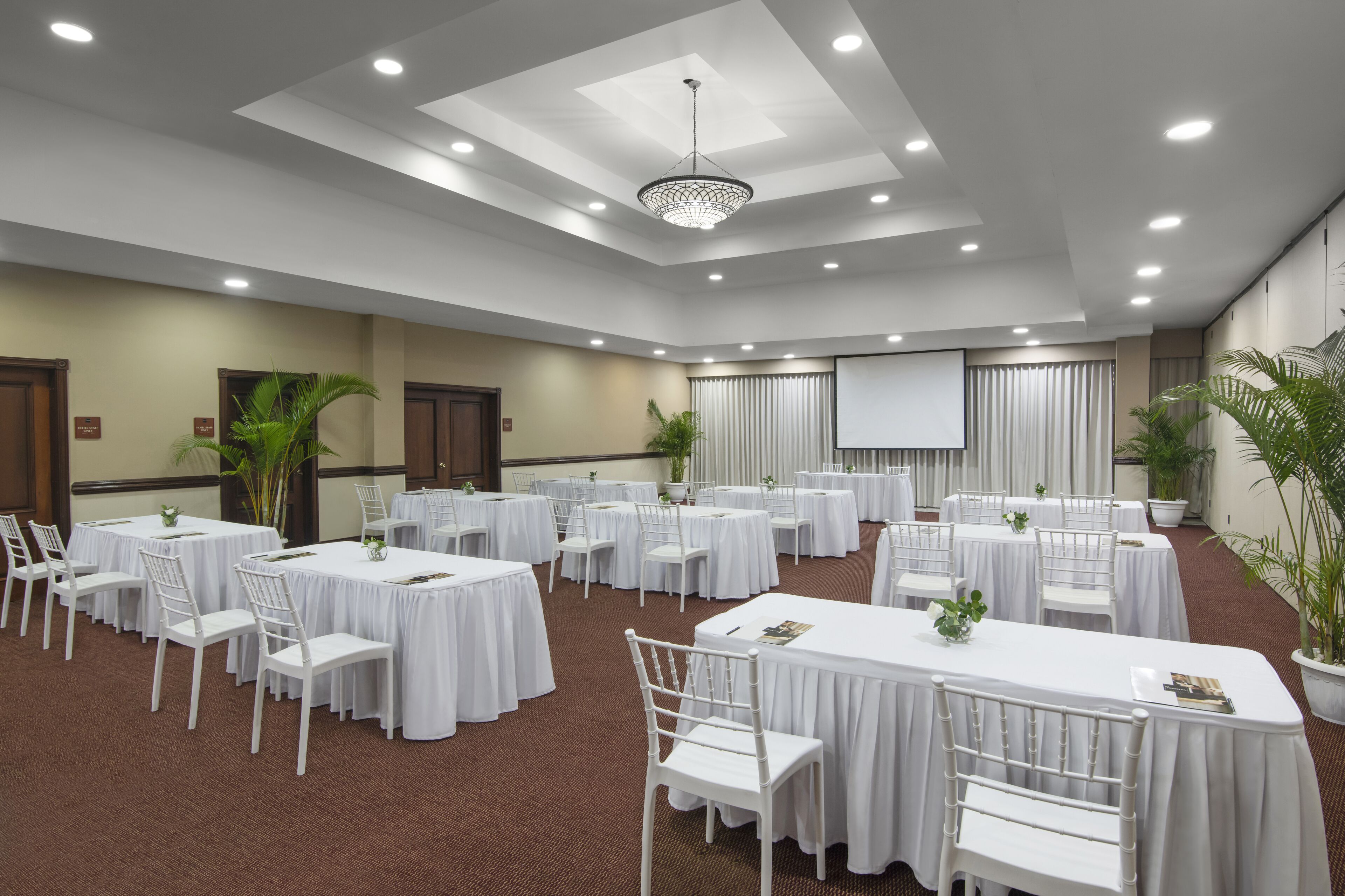 A conference room with multiple round tables, white chairs, and a large screen.