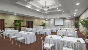 A conference room with multiple round tables, white chairs, and a large screen.