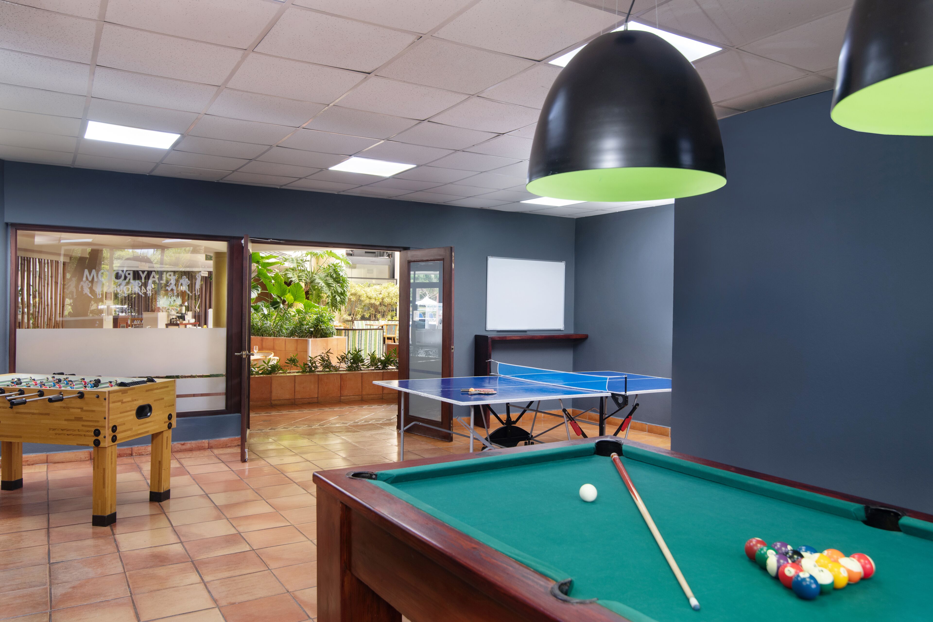 A billiards room with a pool table, a foosball table, and a ping pong table.