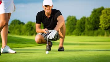Een persoon in een zwart polo shirt en geruit korte broek op een golfbaan, die zich klaarmaakt om te putten.