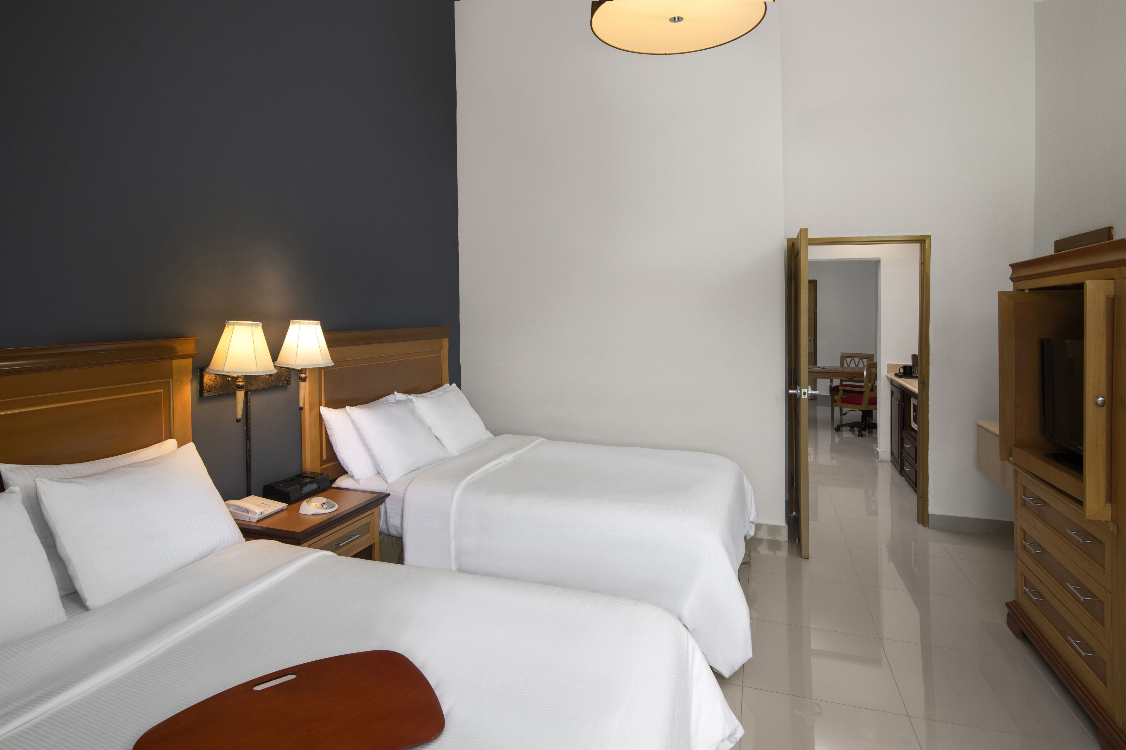 Habitación de hotel con dos camas, un aparador de madera, televisión y escritorio con lámparas.