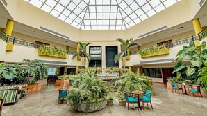 Un vaste atrium doté d’un haut plafond et d’une coupole de verre, comprenant plusieurs niveaux avec des espaces de repos et une végétation intérieure luxuriante.