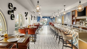 A restaurant with a long counter, multiple tables, and a patterned floor. - Hayes Mansion, San Jose - Curio Collection by Hilton (San Jose)