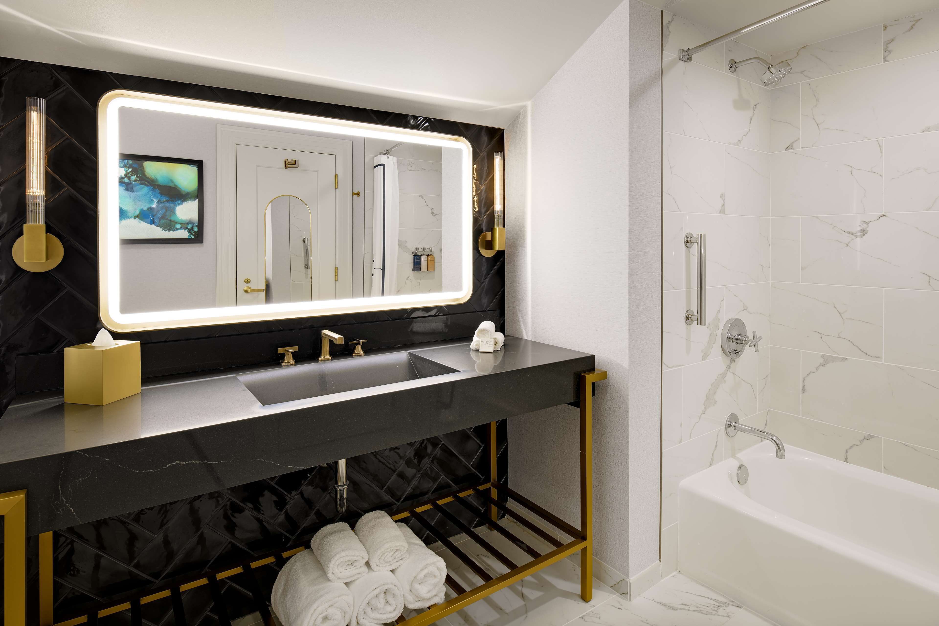 A modern bathroom with a large mirror, a sink, and a bathtub.