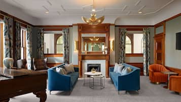 A spacious living room with a grand piano, two blue sofas, a fireplace, and a chandelier.