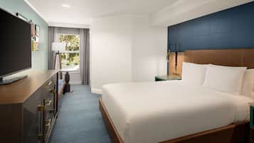A hotel room with a large bed, a desk with drawers, a television, and a window with curtains.