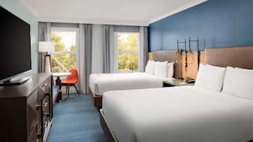 A hotel room with two beds, a desk, a chair, and a TV.