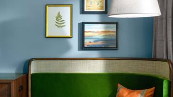A room with a green sofa, a round table, and a lamp. There are framed pictures on the wall.