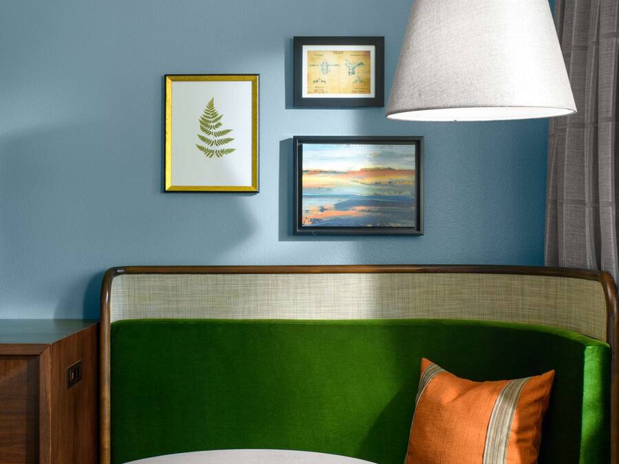 A room with a green sofa, a round table, and a lamp. There are framed pictures on the wall.
