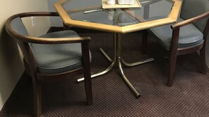 A round glass table with a wooden frame, accompanied by two upholstered chairs with metal legs. - AmeriVu Inn & Suites (Wolcott)