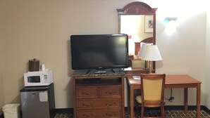 A hotel room with a television, a microwave, a refrigerator, a wooden dresser, a desk, a chair, and a lamp. - AmeriVu Inn & Suites (Wolcott)