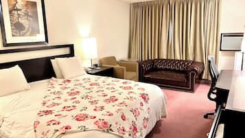 A hotel room with a bed, a desk, a chair, a sofa, a lamp, and a window with curtains.