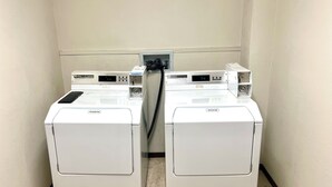 A laundry room with two front-loading washing machines and a dryer. - Americas Best Value Inn Laramie (Laramie)