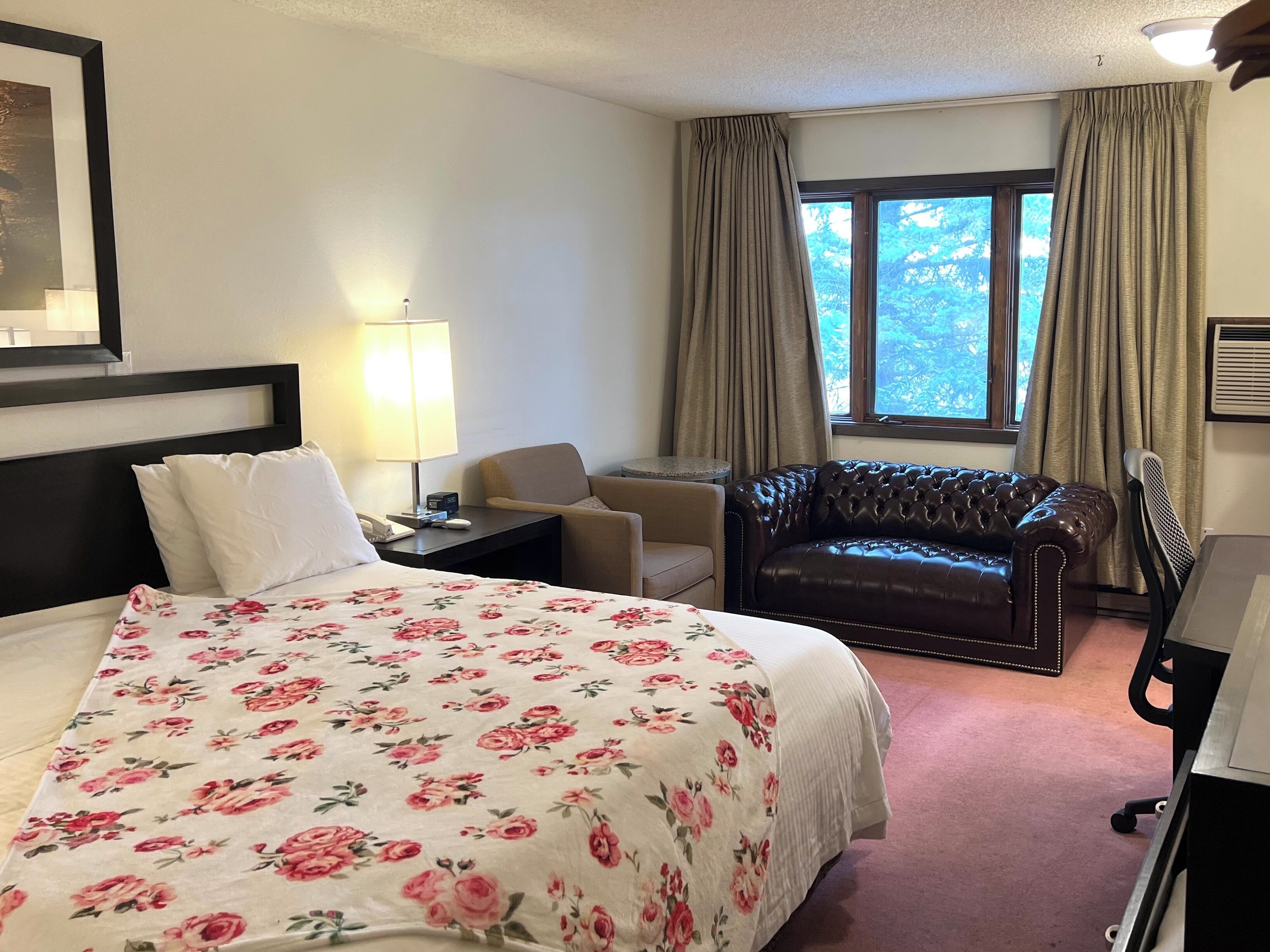 A hotel room with a bed, a chair, a leather sofa, a desk, and a window with curtains.