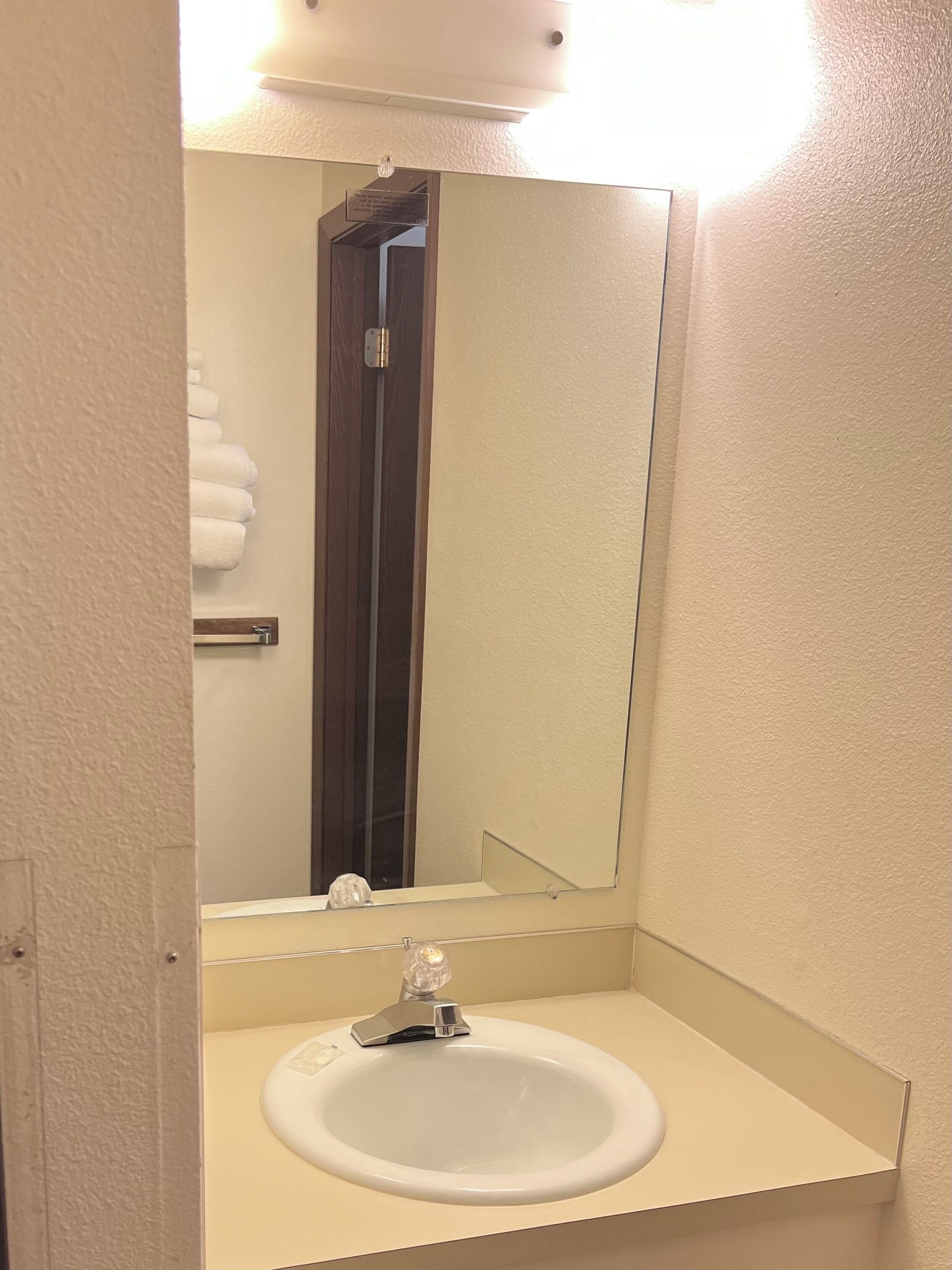 Un baño con un lavabo blanco, un espejo y un perchero para toallas.