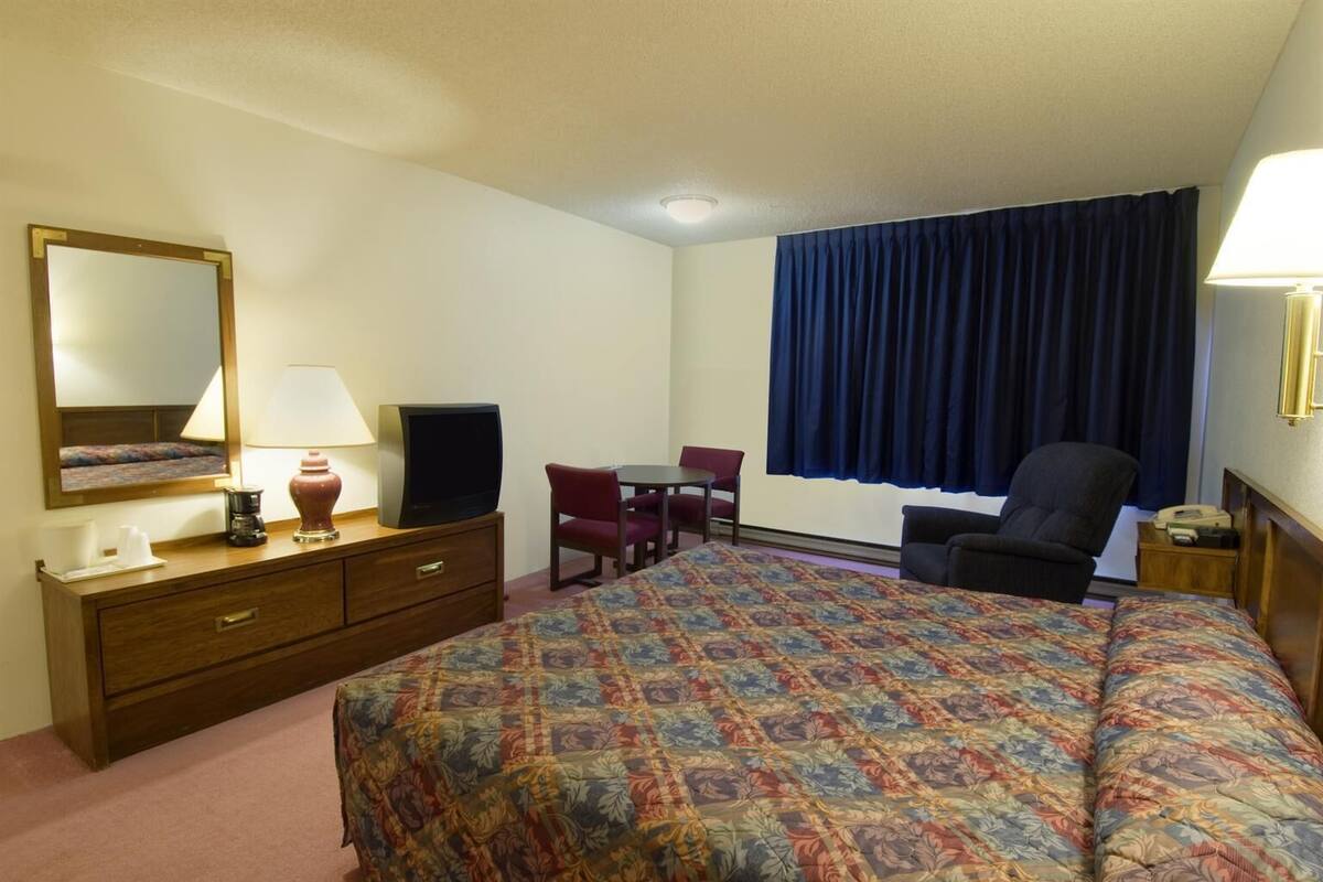 A hotel room with a bed, a desk, a chair, a television, a lamp, and a large window with curtains.