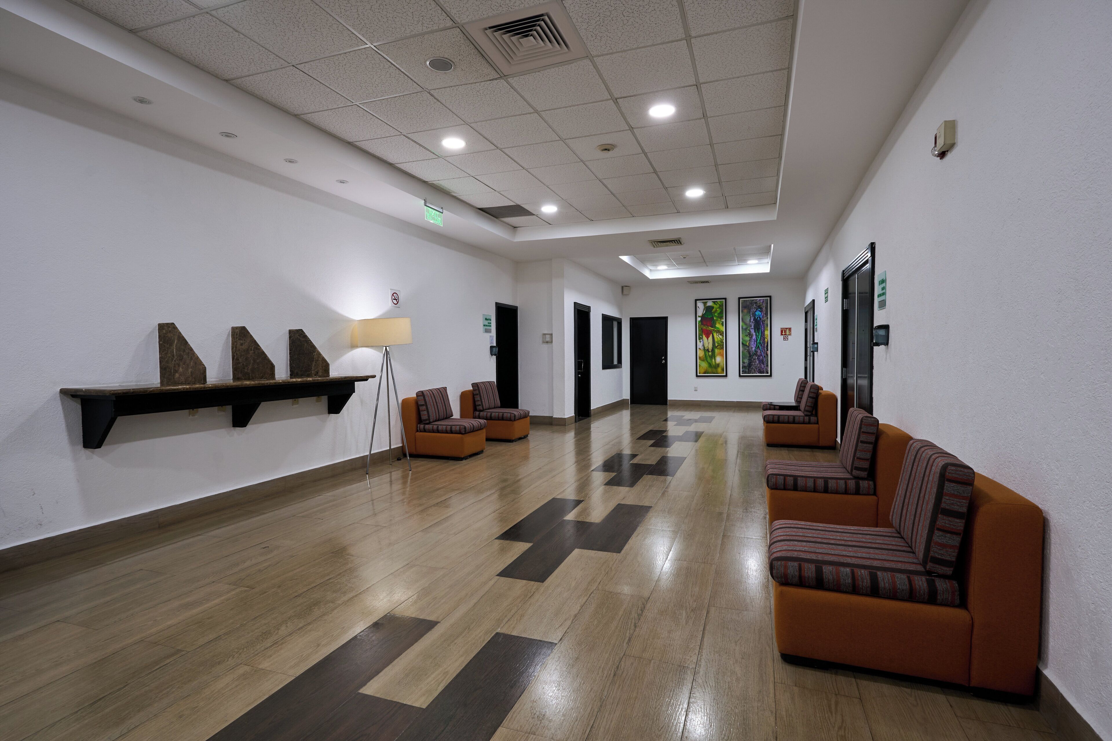 A spacious lobby with a wooden floor, several sofas, a lamp, and artwork on the walls.