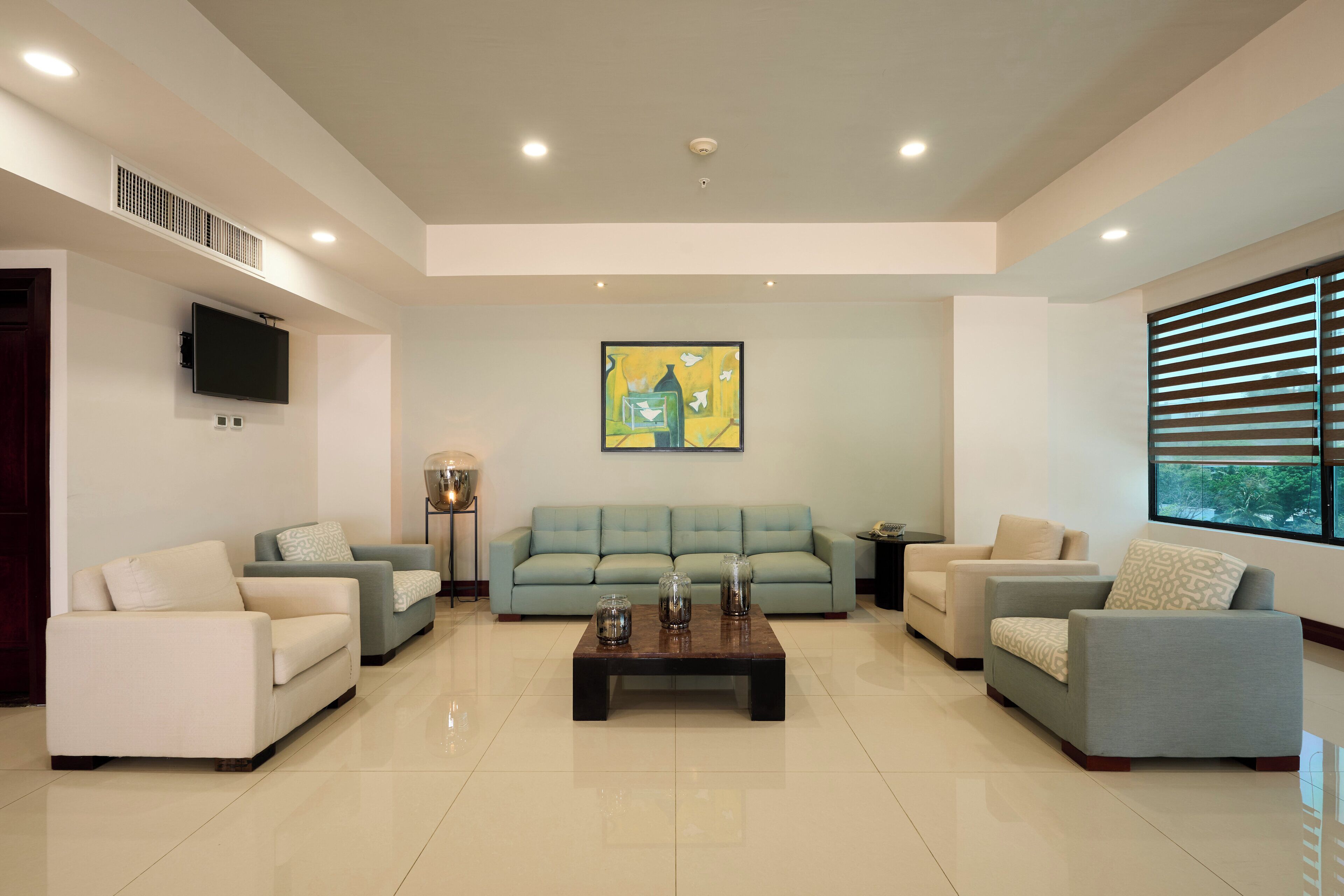 Uma sala de estar espaçosa com um amplo sofá azul claro, duas poltronas, uma mesa de centro e uma TV de tela plana na parede.