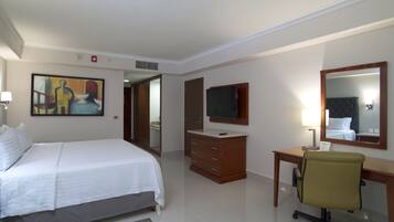 A hotel room with a bed, a desk with a chair, a television, a mirror, and a painting on the wall.