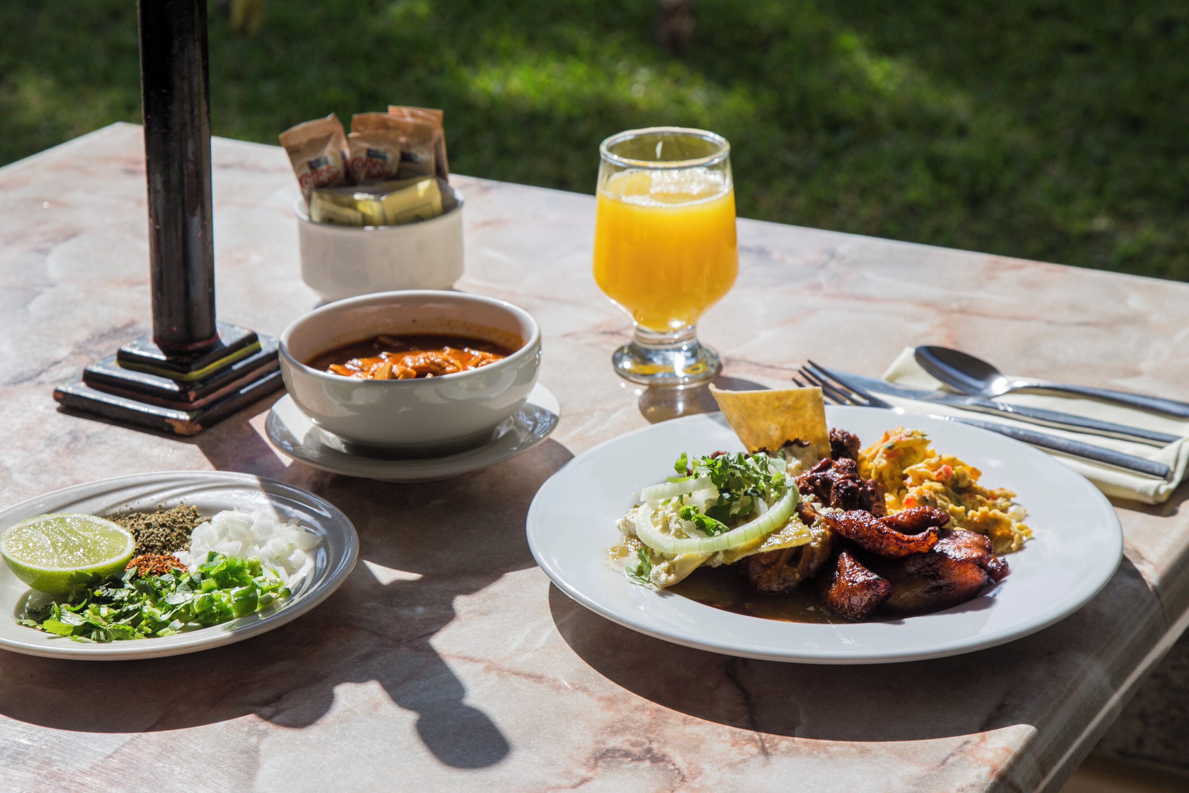 Une table dressée avec un repas composé de viande, de légumes et d’un verre de jus d’orange.