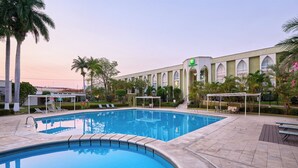 A swimming pool with lounge chairs and a building with arched windows in the background. - Holiday Inn Tuxtla Gutierrez by IHG (Tuxtla Gutierrez)