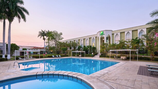 A swimming pool with lounge chairs and a building with arched windows in the background. - Holiday Inn Tuxtla Gutierrez by IHG (Tuxtla Gutierrez)