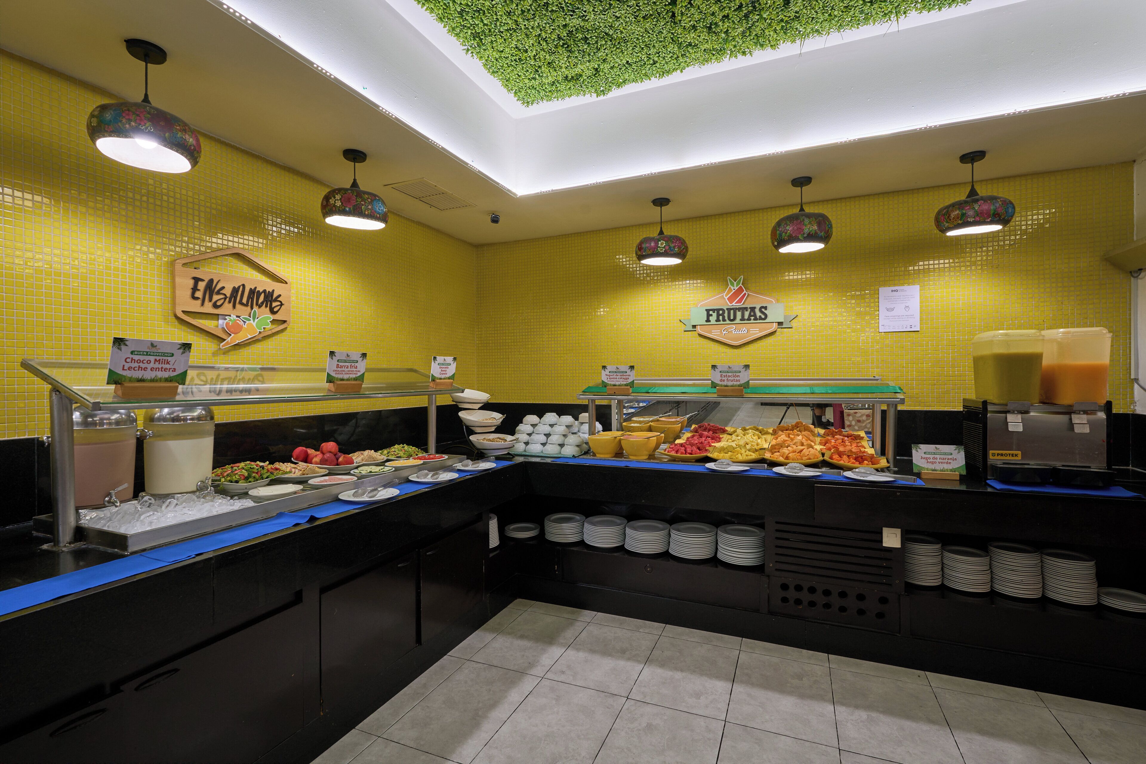 Un espace buffet avec différents stands de nourriture, dont un panneau indiquant « Ensalmons » et « Frutas ».