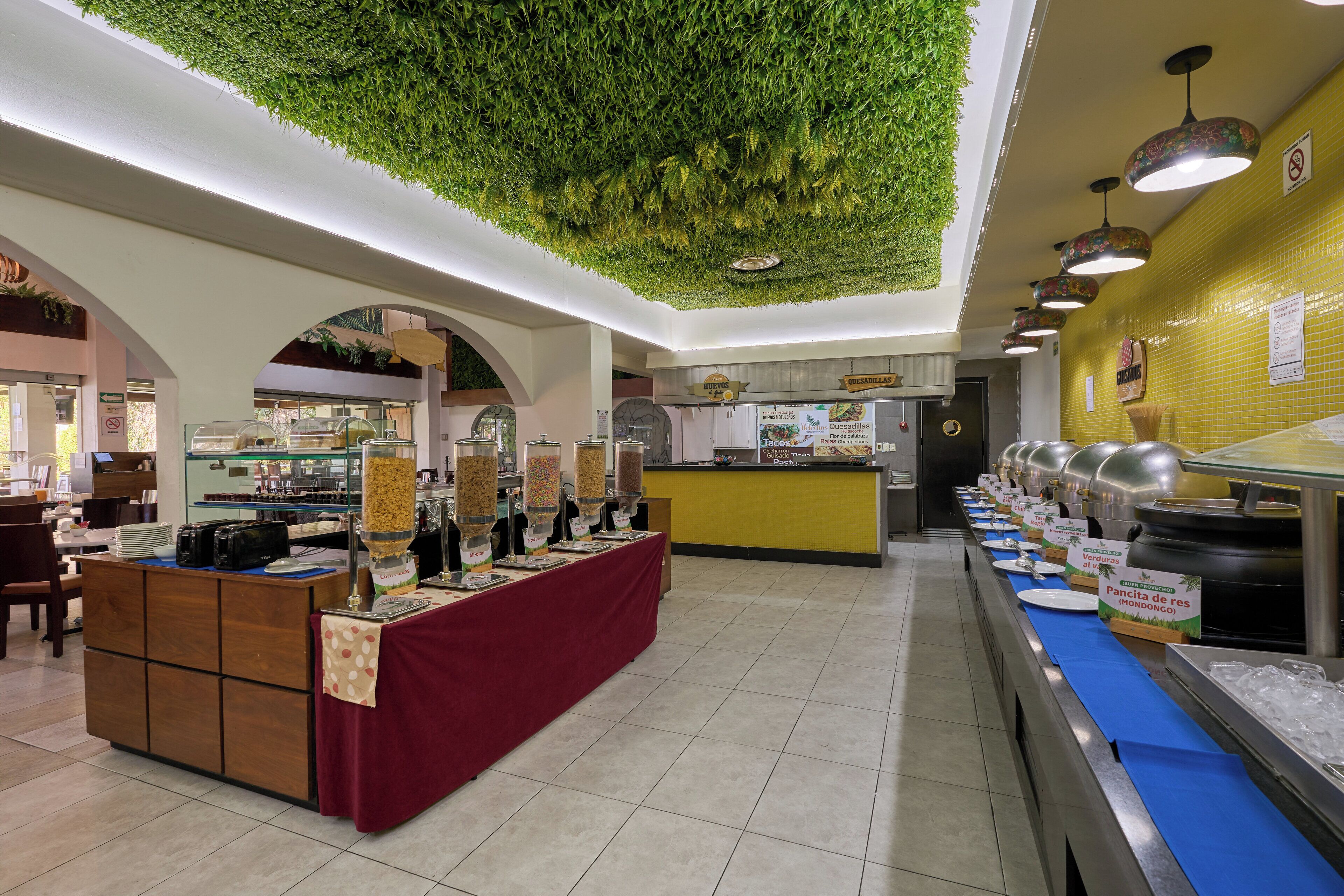 Un espace buffet avec un plafond vert, un comptoir recouvert d’une nappe rouge et différents stands de nourriture.
