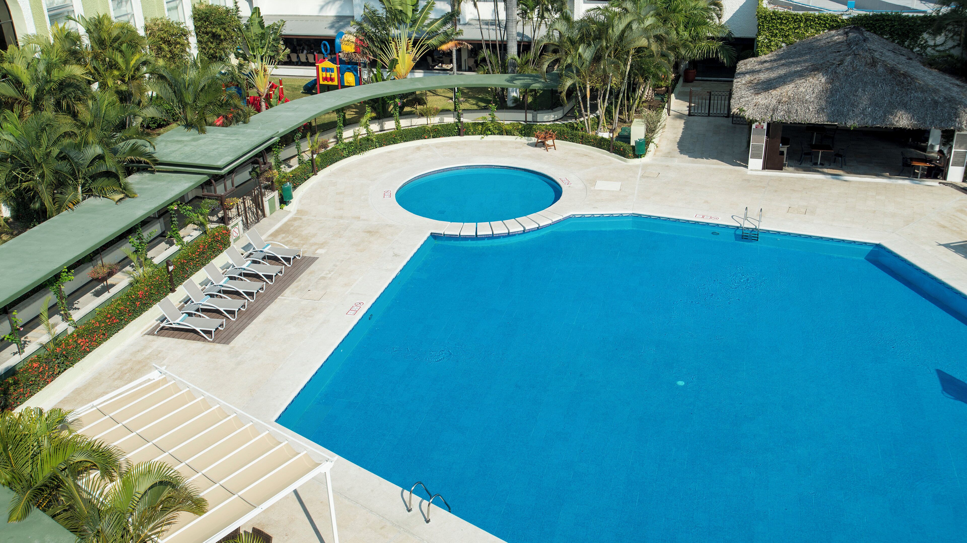 A large swimming pool with a sun deck, lounge chairs, and a children's play area.